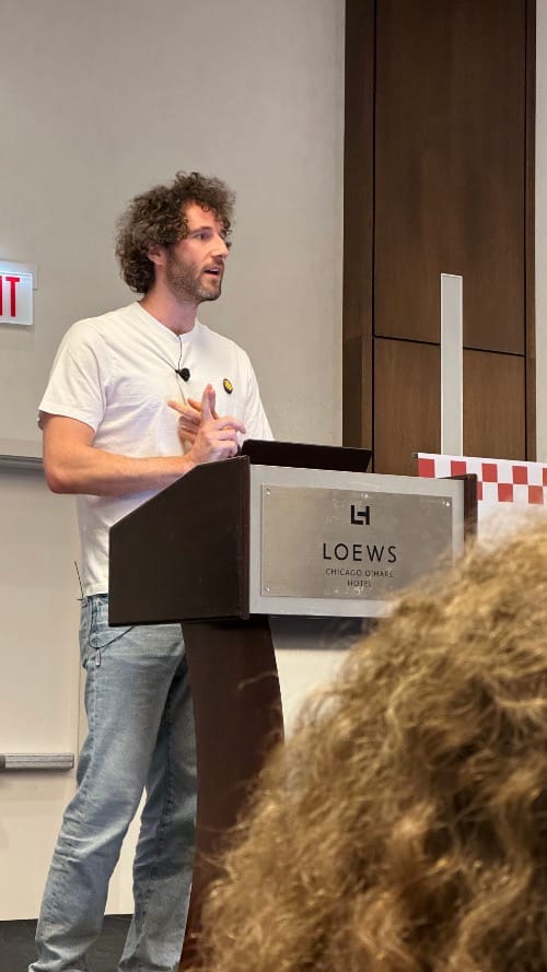 Jordi Bruin standing behind a wood podium. He is looking slightly to his left.